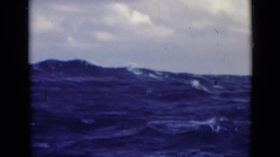 Rough blue sea with small whitecaps and a cloudy horizon, showing visible grain and color shift from archival 8mm film.