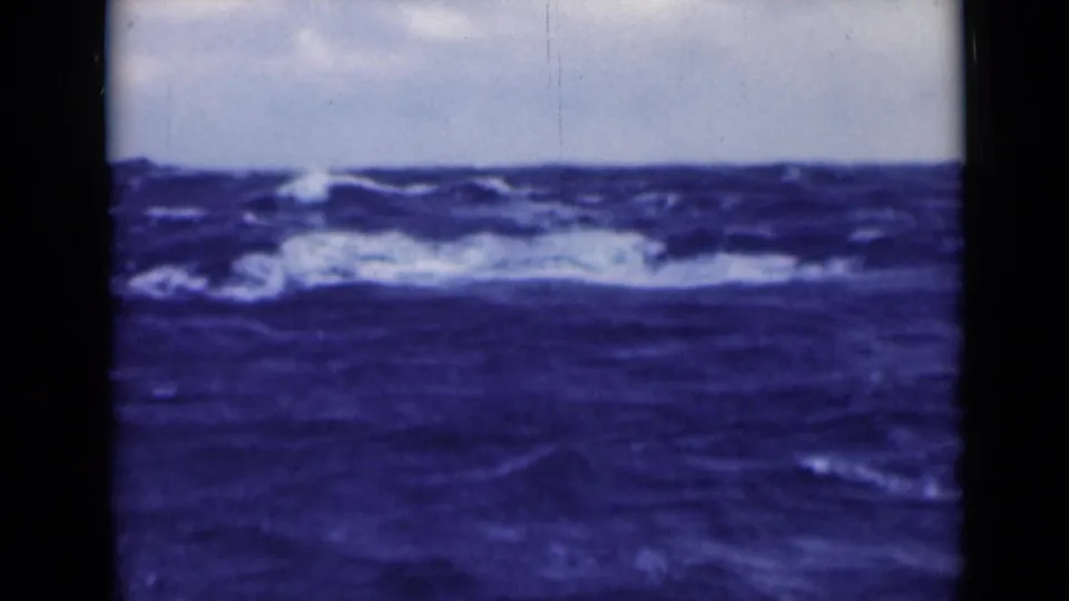 1940s 8mm frame showing churning open water, white foam near the horizon, and blue-tinted film color.