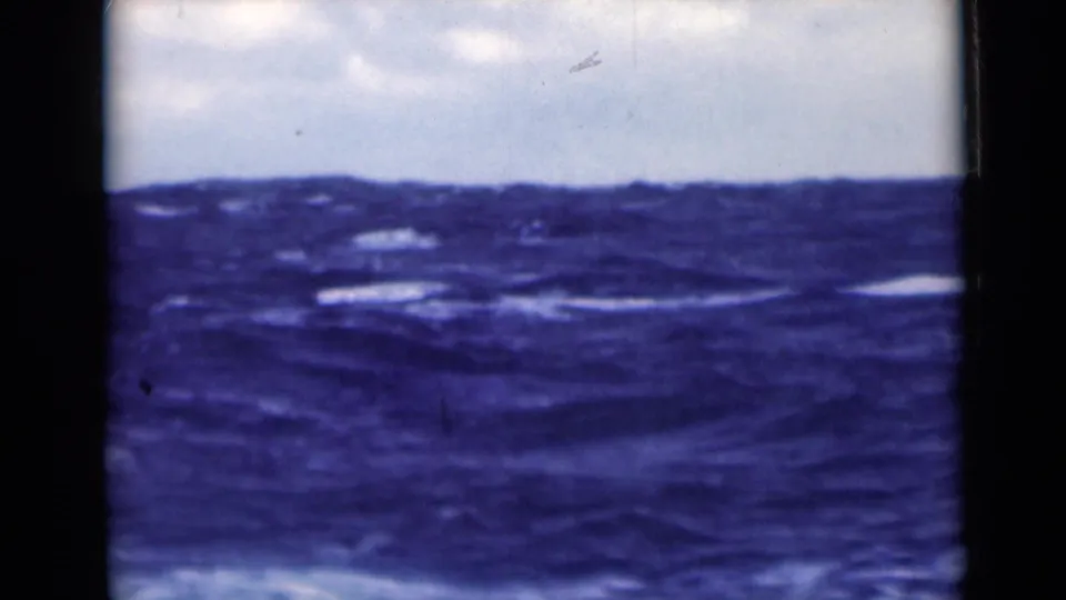 1940s 8mm frame of rough open water under a pale sky, with white foam streaks and visible film wear.