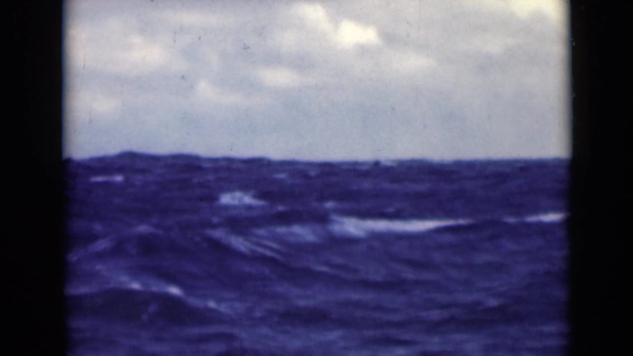 Dark blue ocean swells under a cloudy sky, framed by black film edges.