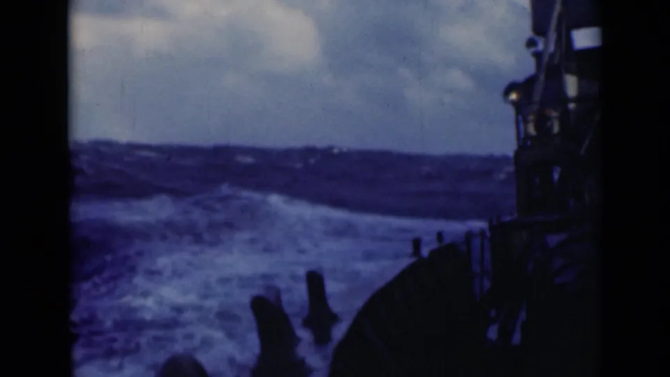 A dark ship rail and deck structure frame foaming waves in this 1947 8mm shipboard scene.