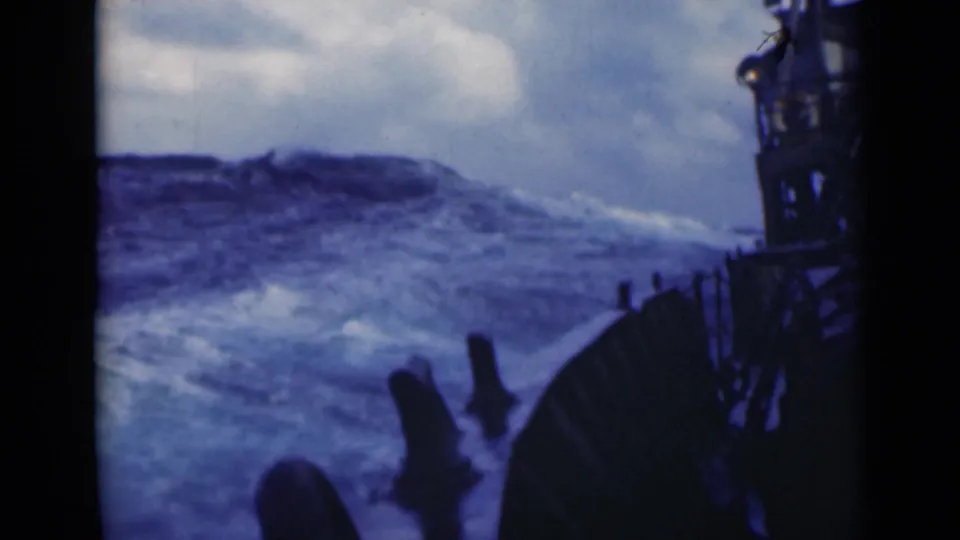 The vessel's dark railing is visible beside a rising swell and white foam in rough open water.