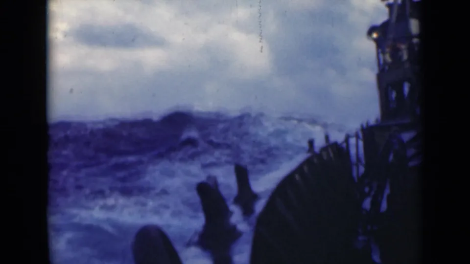 1947 8mm shipboard footage shows turbulent blue water, spray, railings, and silhouetted deck structure beneath a cloudy sky.