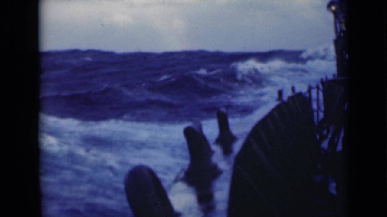 Rough sea ahead of a large ship, with railings and dark ship structure at the right edge.