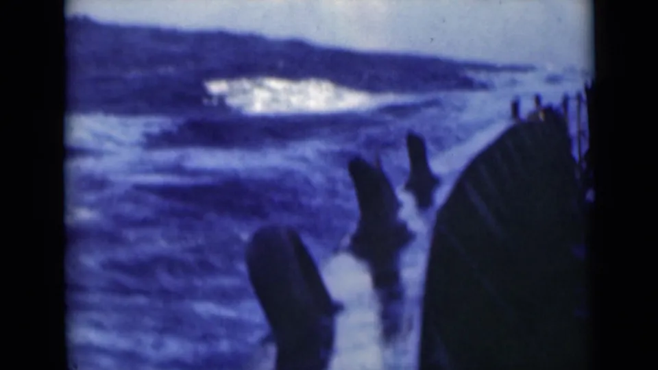 1940s 8mm shipboard view of heavy blue seas and whitecaps beyond dark railings and deck equipment.