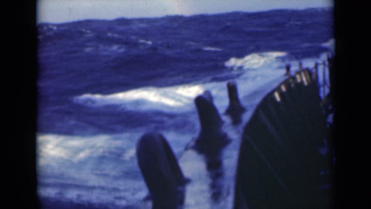 Foaming waves roll beside a ship deck with dark railings in the foreground.
