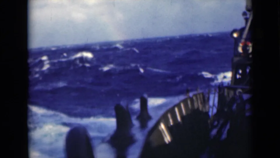 Heavy ocean swell viewed from a ship deck, with soft 8mm color and dark vessel hardware at the frame edge.