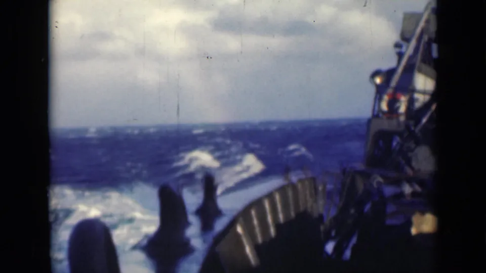 Final shipboard view of rough seas, deck railing, and distant horizon in soft, grainy 8mm color footage.