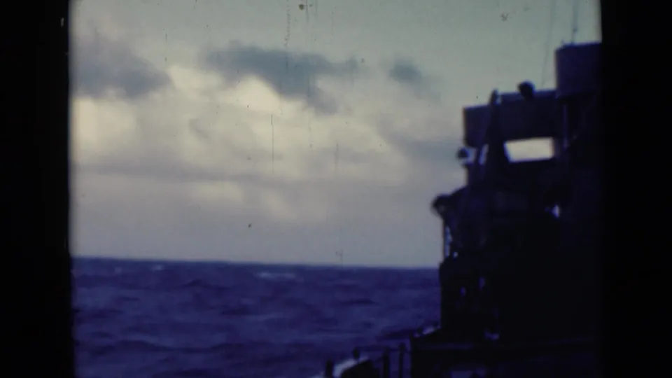 1947 8mm shipboard view of choppy water and whitecaps, with a dark deck structure at right and clouds over the horizon.