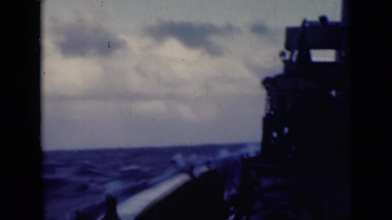 1940s 8mm home-movie frame showing rough open water, a cloudy horizon, and a shadowed ship deck along the right side.