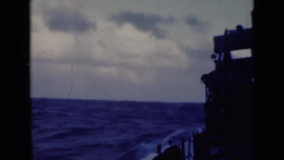 Choppy open water and overcast sky seen from an onboard viewpoint, with the vessel's dark deck occupying the right side.