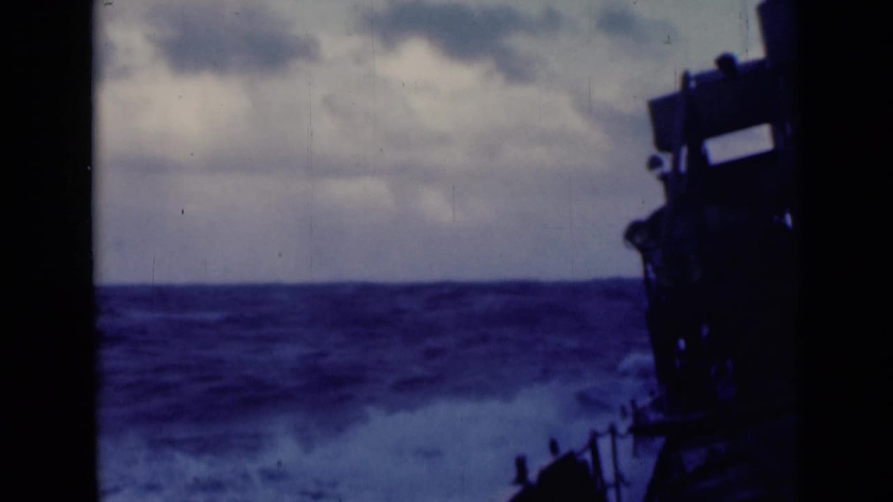 Rough sea and whitecaps seen from a ship deck with dark structure at right.
