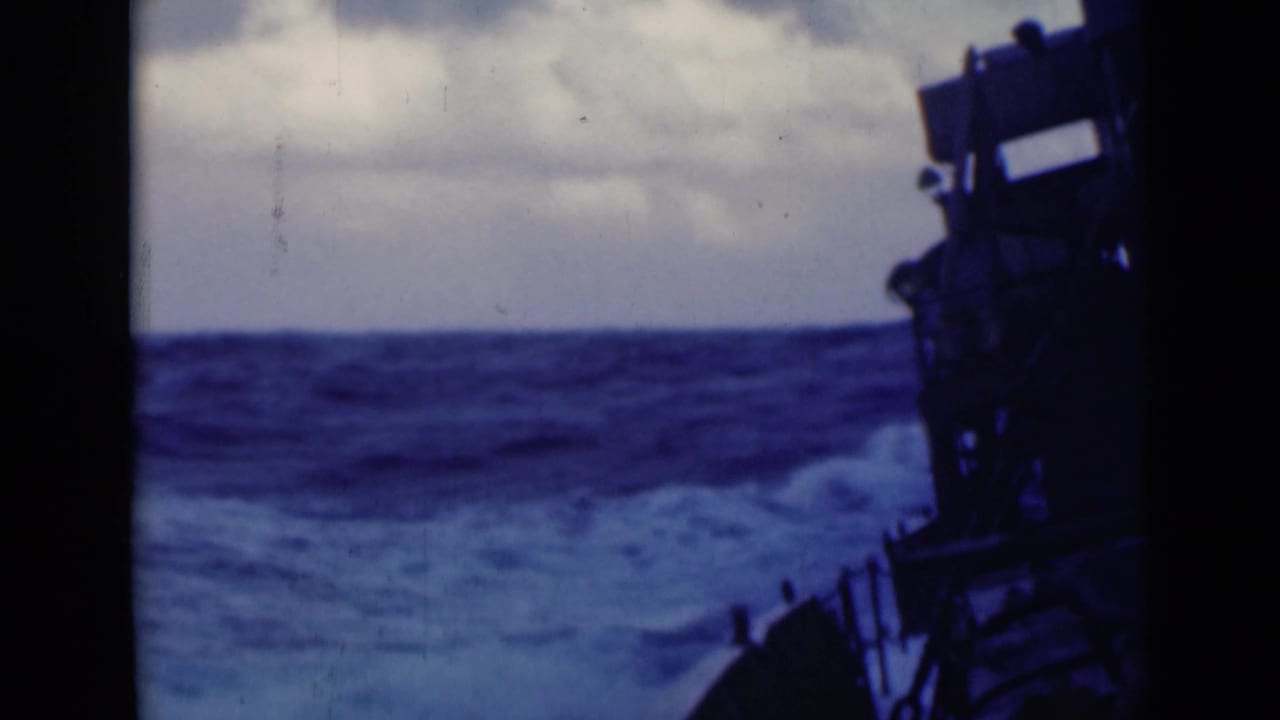 Large waves rise beyond a dark ship structure and deck edge.