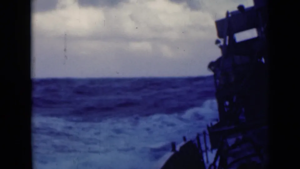 A rough open sea fills the frame, with white spray and part of the ship silhouetted at the right in 8mm home-movie footage.