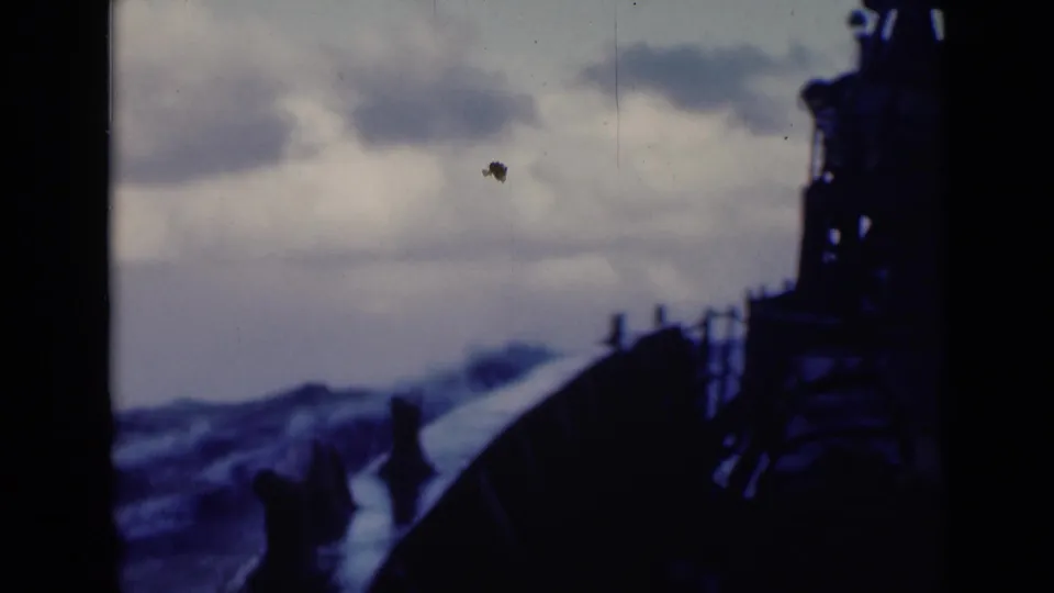 Deck-level 8mm view of a large vessel's bow cutting through rough blue sea beneath heavy clouds.