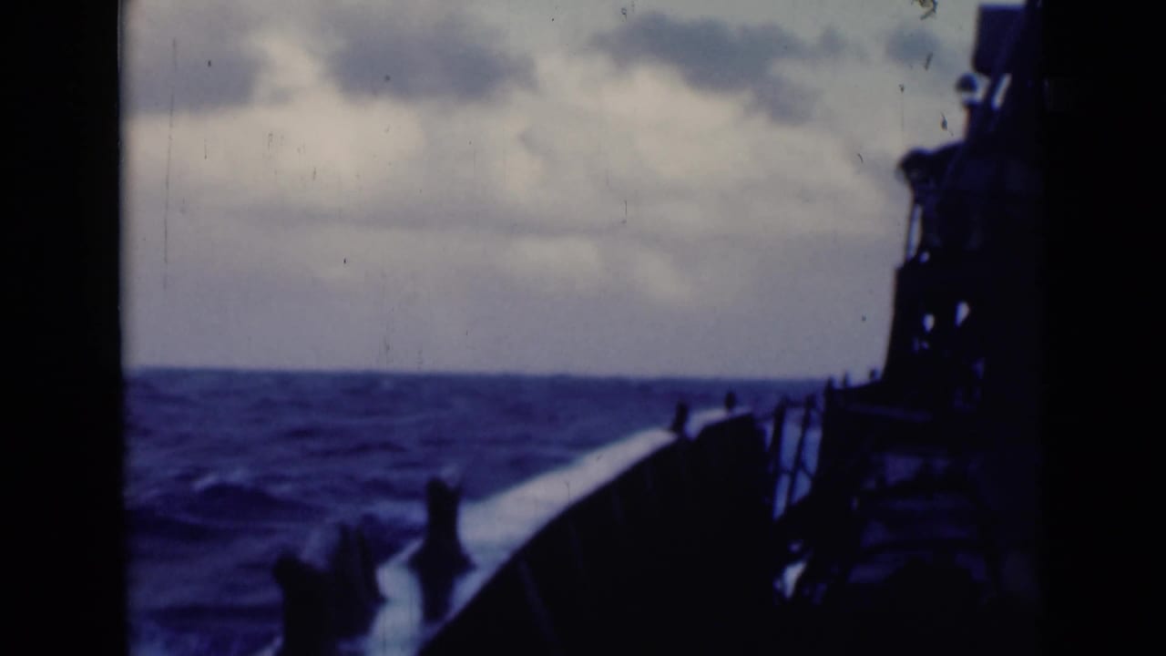 Bow rail and dark ship structure pass through choppy sea beneath clouds.