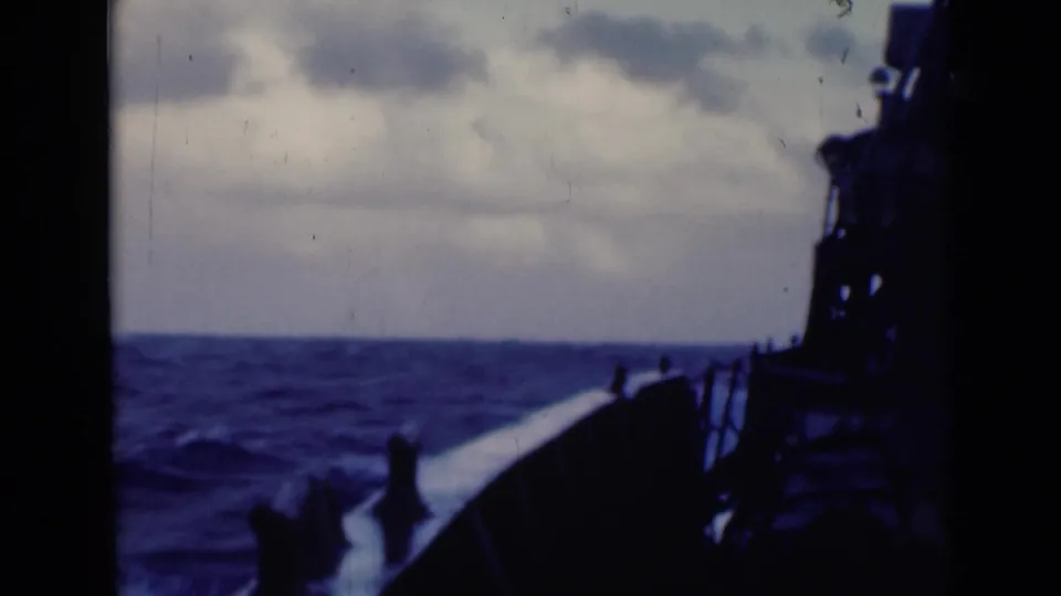 Forward view from a ship deck shows railings, dark superstructure, and rough open water in soft 8mm color.