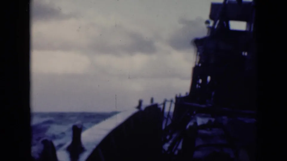 The vessel's bow and railings lead into choppy blue water, with dark ship machinery silhouetted at right.