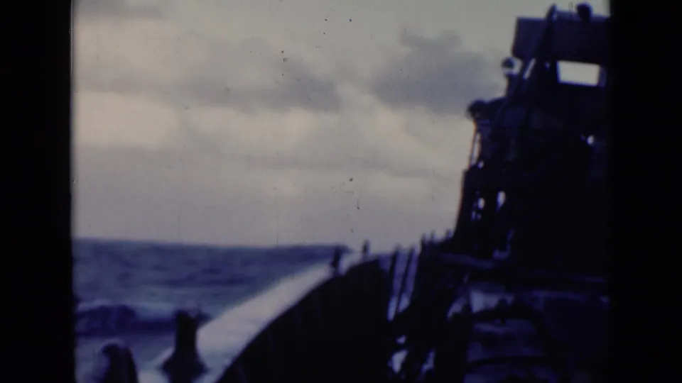 1947 8mm frame from a shipboard viewpoint, looking past the deck toward choppy water and a dark superstructure silhouette.