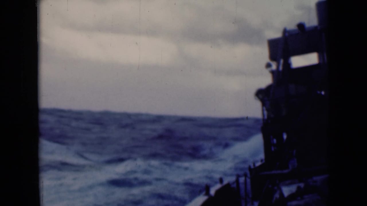 Rough blue sea seen from a ship deck with a dark structure at right.