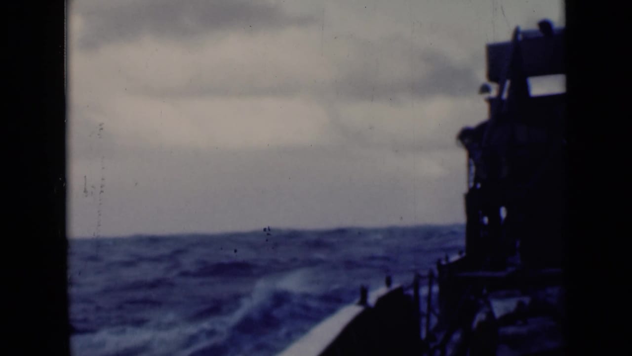 Ship bow area and dark deck equipment face choppy waves under cloud cover.