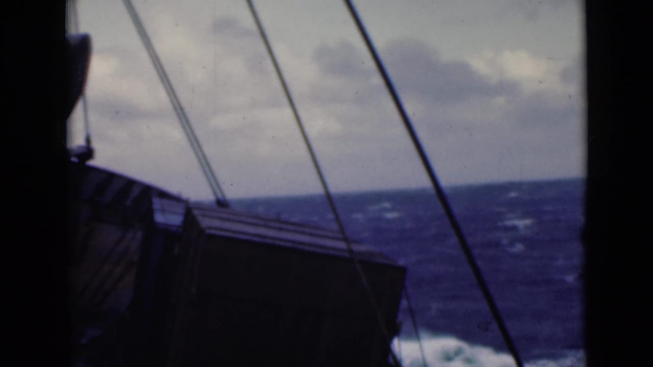 Ship rigging and deck structure seen against rough water and cloudy sky.