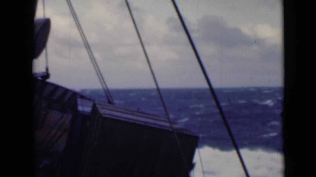 Rigging lines cross a view of the ship side and choppy open water.