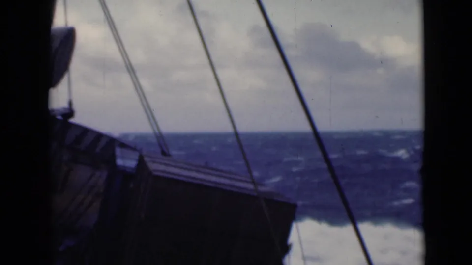 Deck-level 8mm view of a ship structure and rigging with choppy blue water and low clouds beyond.