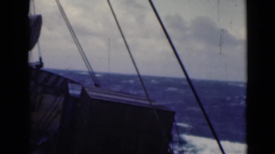 Soft 8mm frame showing a dark section of ship, diagonal rigging, rough sea, and cloudy horizon.