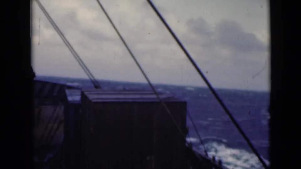 Final 8mm frame of ship rigging and a dark deck edge with rough water, white spray, and a cloudy horizon.