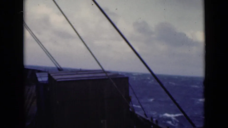 1947 8mm shipboard view through a cabin window, showing diagonal rigging, a dark deck structure, and rough sea under clouded sky.