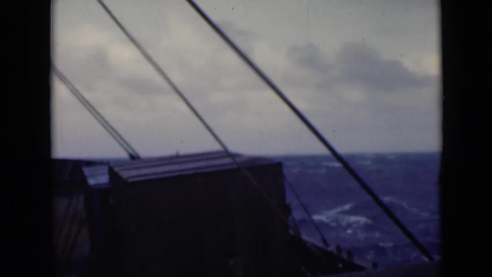 Shipboard 8mm frame looking past dark deck equipment and rigging toward rolling open water in stormy weather.