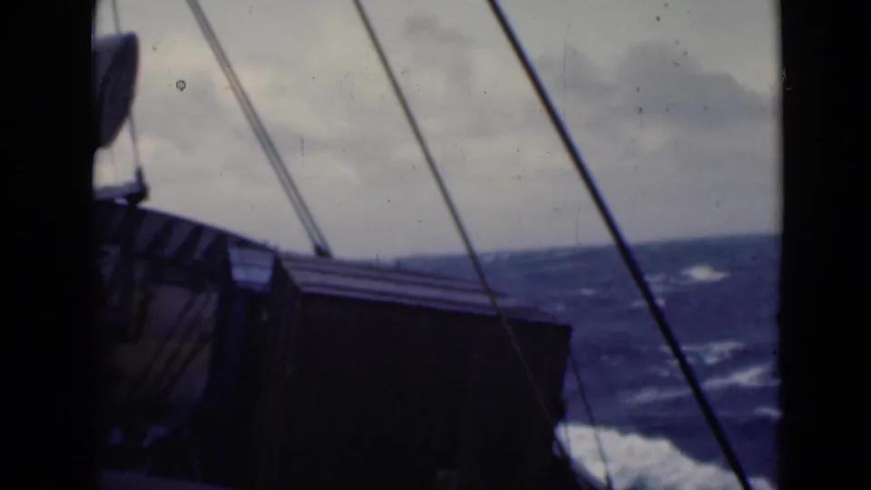 1947 8mm deck view of a ship at sea, with rigging and dark railings framing rough blue water and clouds.