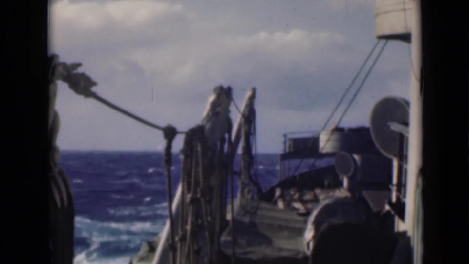 1947 8mm home-movie frame from a vessel deck, showing hanging ropes, rigging, deck equipment, and rough open sea.