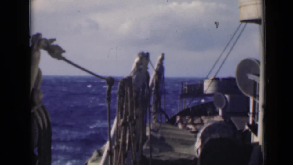 Soft 8mm frame showing vessel deck details and a choppy blue horizon, with ropes and equipment partially obscuring the view.