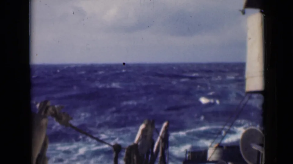 Blue ocean and whitecaps fill the frame, with partial ship rigging and a vertical deck structure visible at the edges.