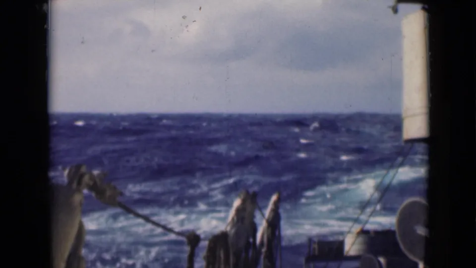 Choppy blue Persian Gulf water seen from a vessel, with foreground rigging, ropes, and rounded deck hardware softened by handheld 8mm filming.