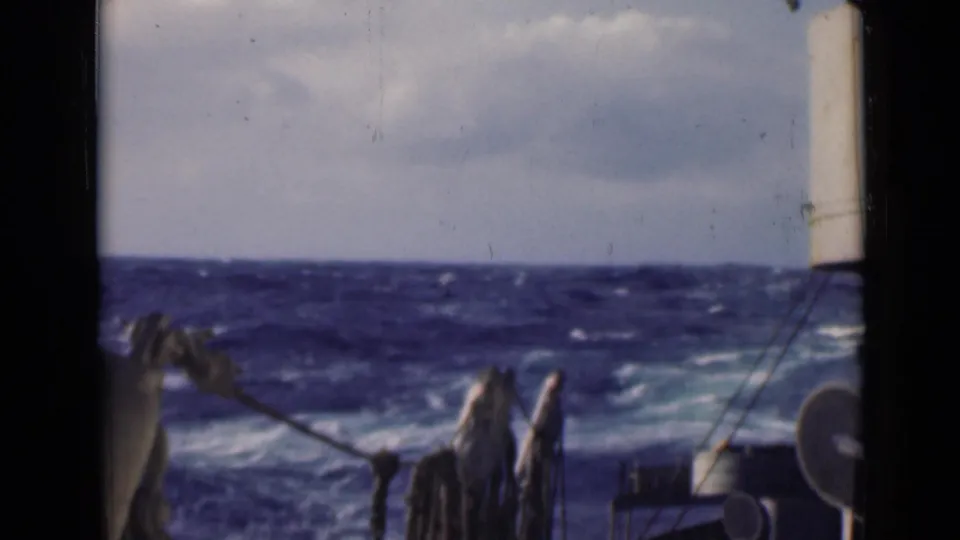 1947 shipboard 8mm frame showing rough open water beyond deck rigging and a white vertical fixture near the bow.