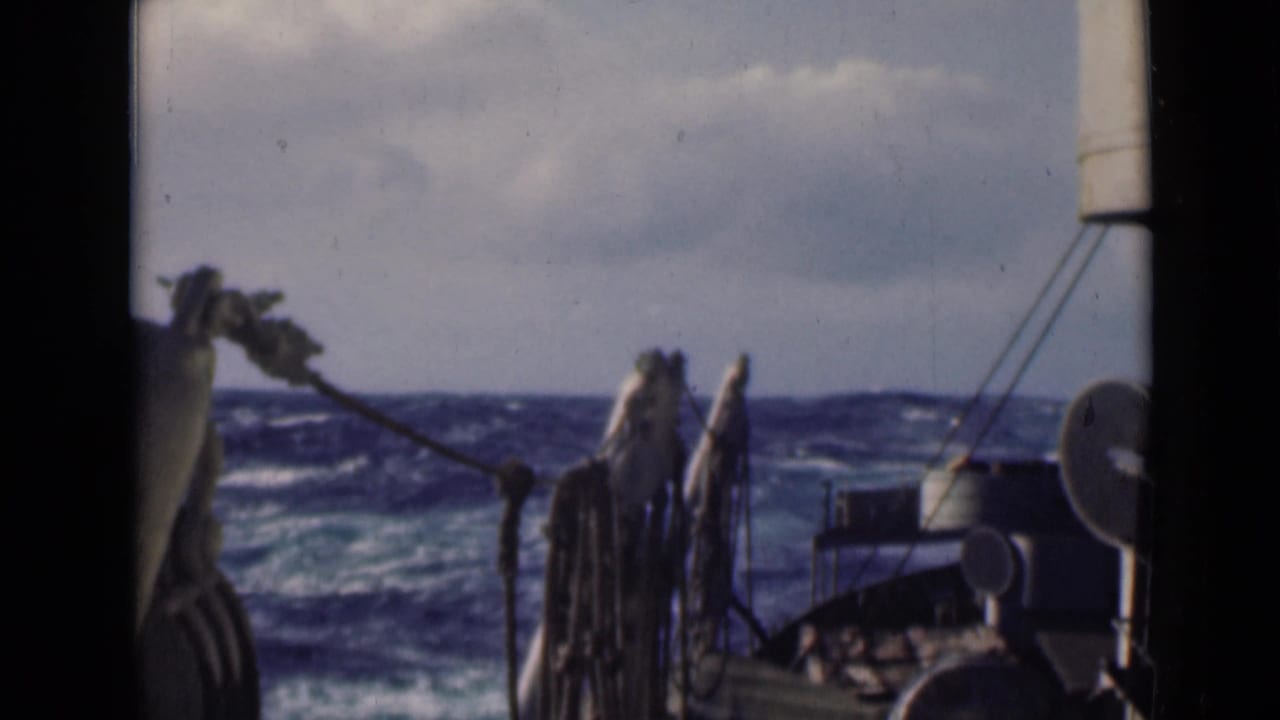 Rough ocean seen past ship deck ropes, railings, and a white deck fixture.