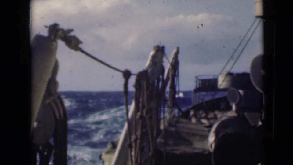Vintage shipboard frame showing ropes and deck structure in the foreground with whitecapped ocean beyond.