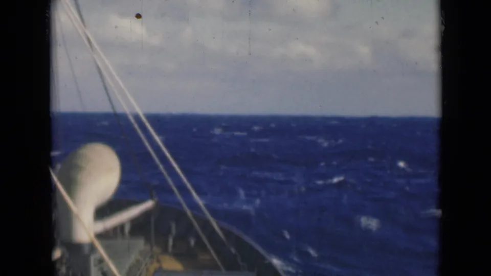 Close shipboard angle with a white dome-like deck feature, rigging, and whitecaps on rough water ahead.
