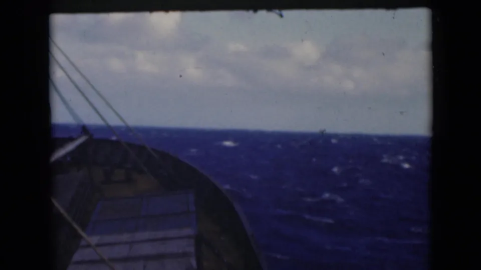 1947 8mm shipboard view of a vessel bow cutting through blue open water beneath a cloudy horizon.