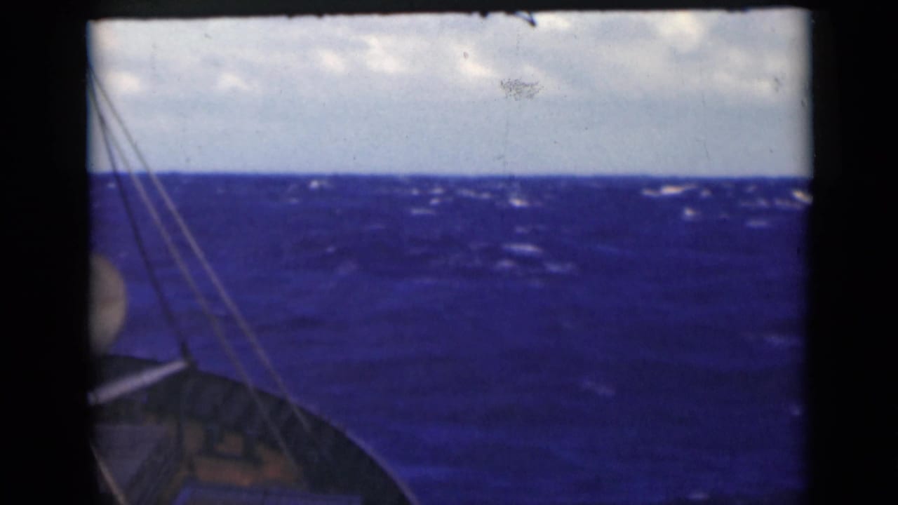 Rough ocean and cloudy horizon with boat rigging visible at the left edge.