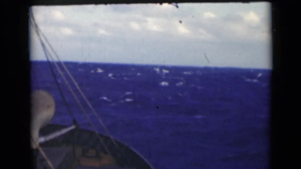 1947 8mm still with a low horizon, choppy blue water, rigging lines, and a small portion of the boat visible at lower left.