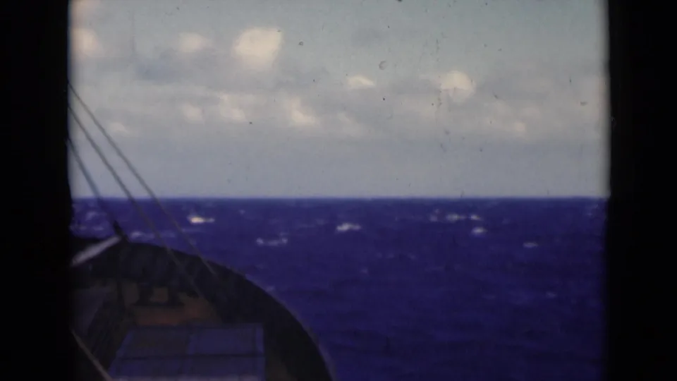 Shipboard 8mm frame looking across deep blue water and whitecaps, with part of the bow and rigging at the left edge.