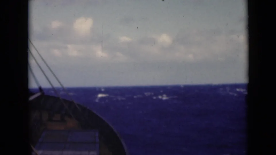 A steady 1947 shipboard view shows blue sea, scattered whitecaps, low bow structure, and cloudy sky within dark 8mm frame edges.