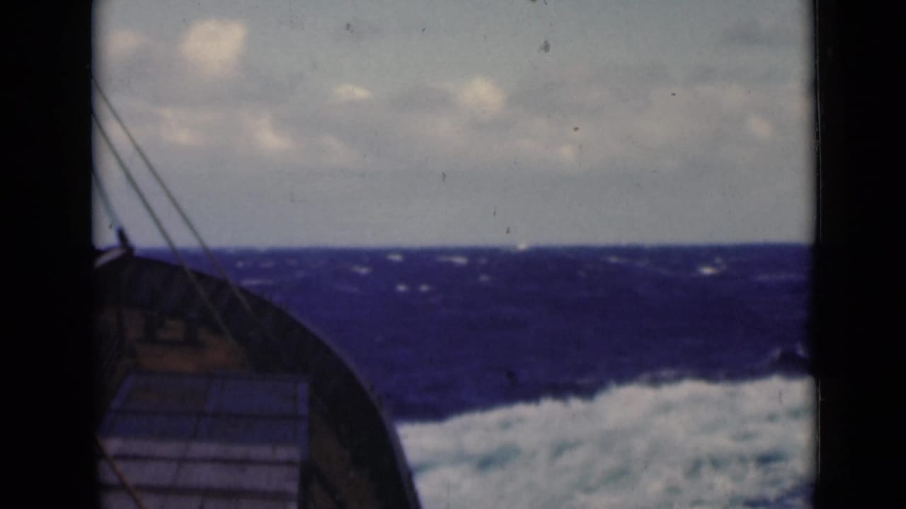 Boat bow and rigging facing choppy blue water under a cloudy sky.