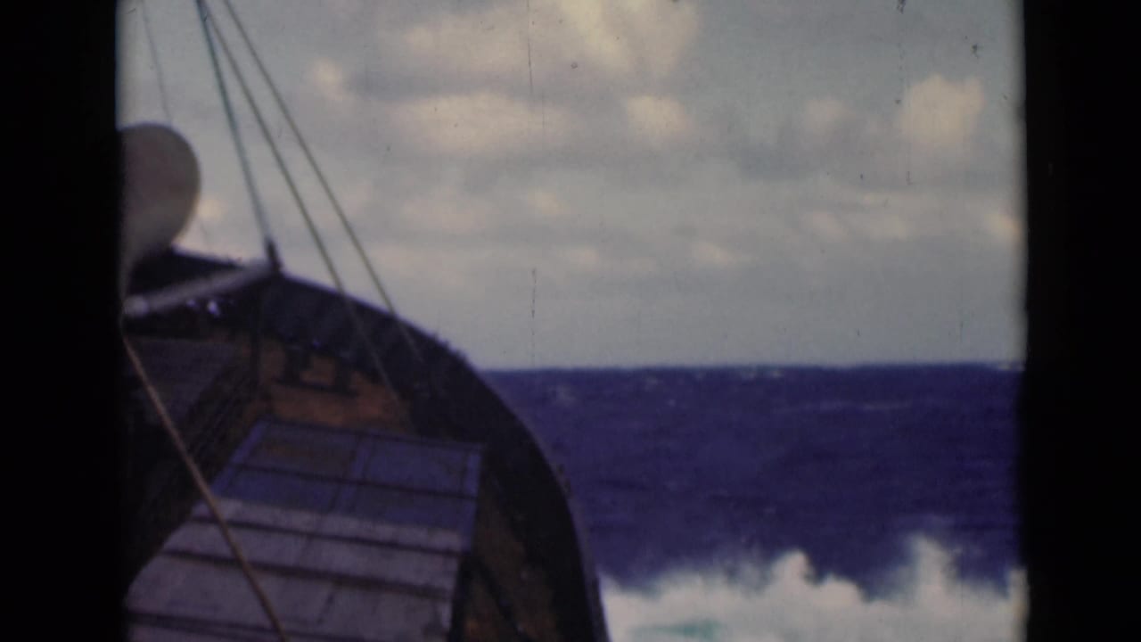 Curved boat bow, rigging, and white surf on rough open water.
