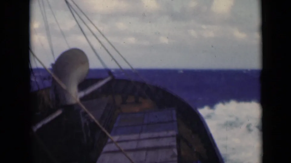 A fixed 8mm deck view shows the bow and rigging of a small boat beside breaking whitecaps under overcast sky.