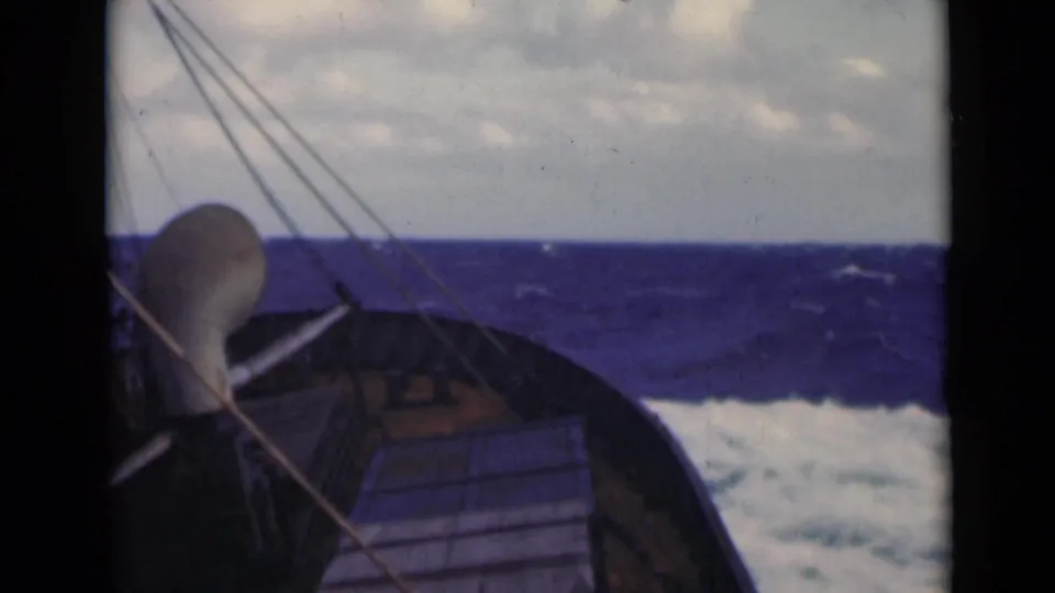 1947 8mm footage shows a sailboat bow, deck edge, and rigging facing choppy open water beneath a cloudy sky.